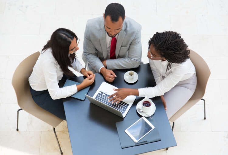 Business team working on laptop during coffee break. Business man and women sitting at table with tablet and cups, using computer and talking. Digital communication concept.
