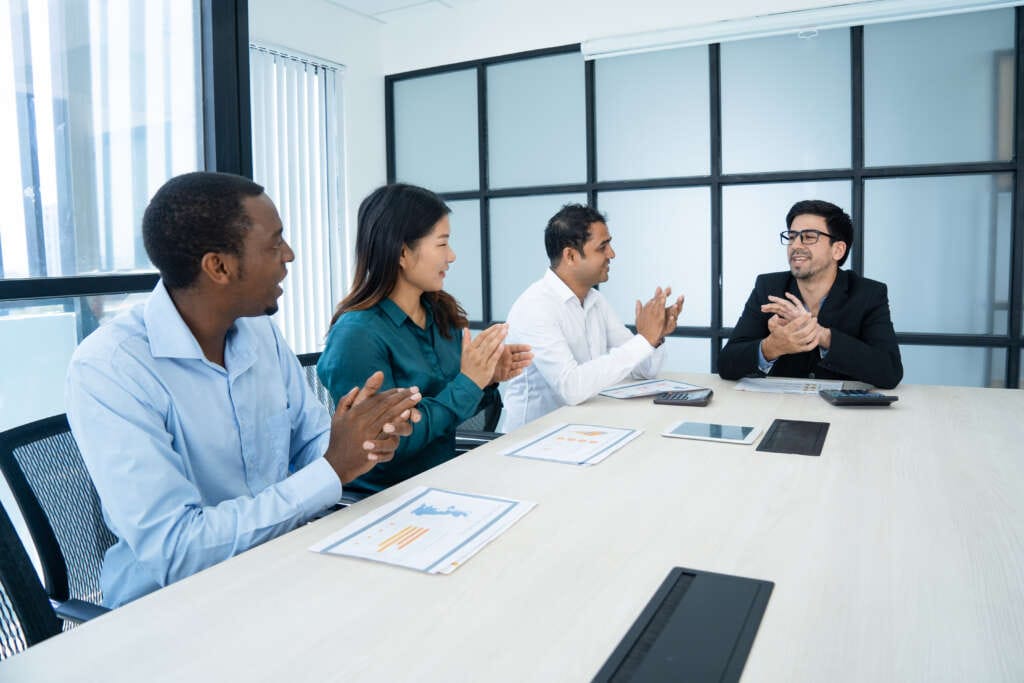 Happy multiethnic employees applauding at meeting while congratulating each other with great results. Positive successful strong business team clapping hands in board room. Employee promotion concept