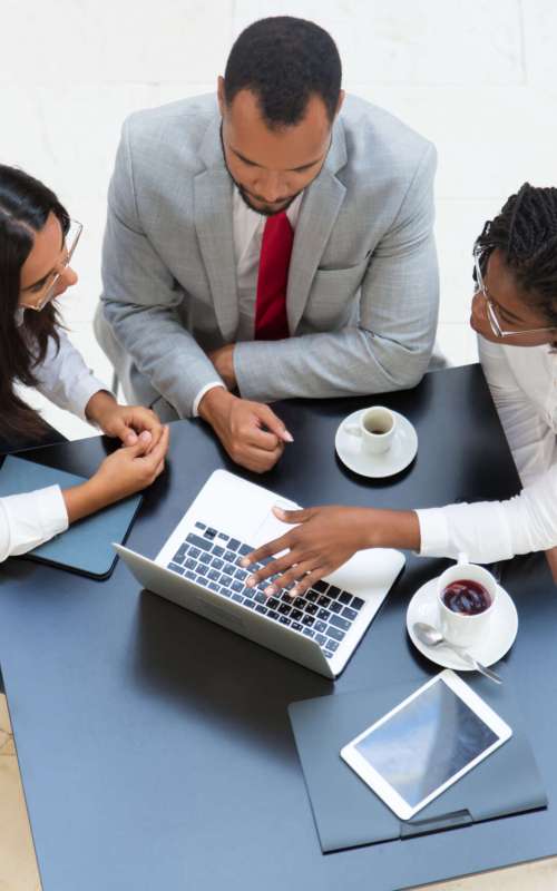 Business team working on laptop during coffee break. Business man and women sitting at table with tablet and cups, using computer and talking. Digital communication concept.